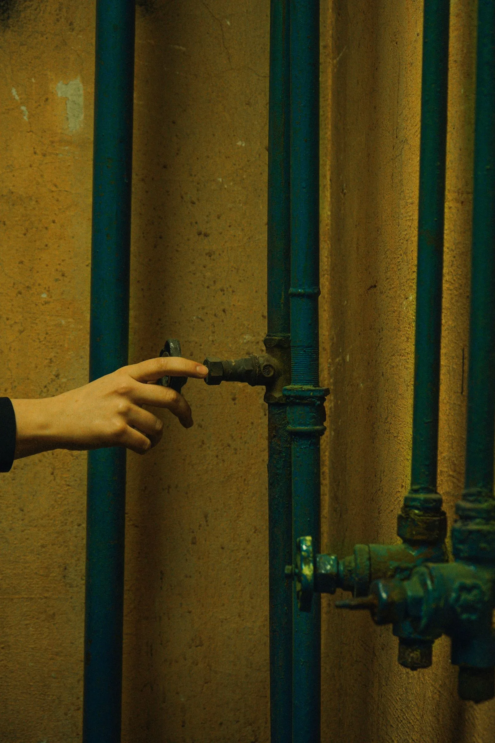 A hand turning a shutoff valve on metal supply pipes during a gas line safety check in a Miami home